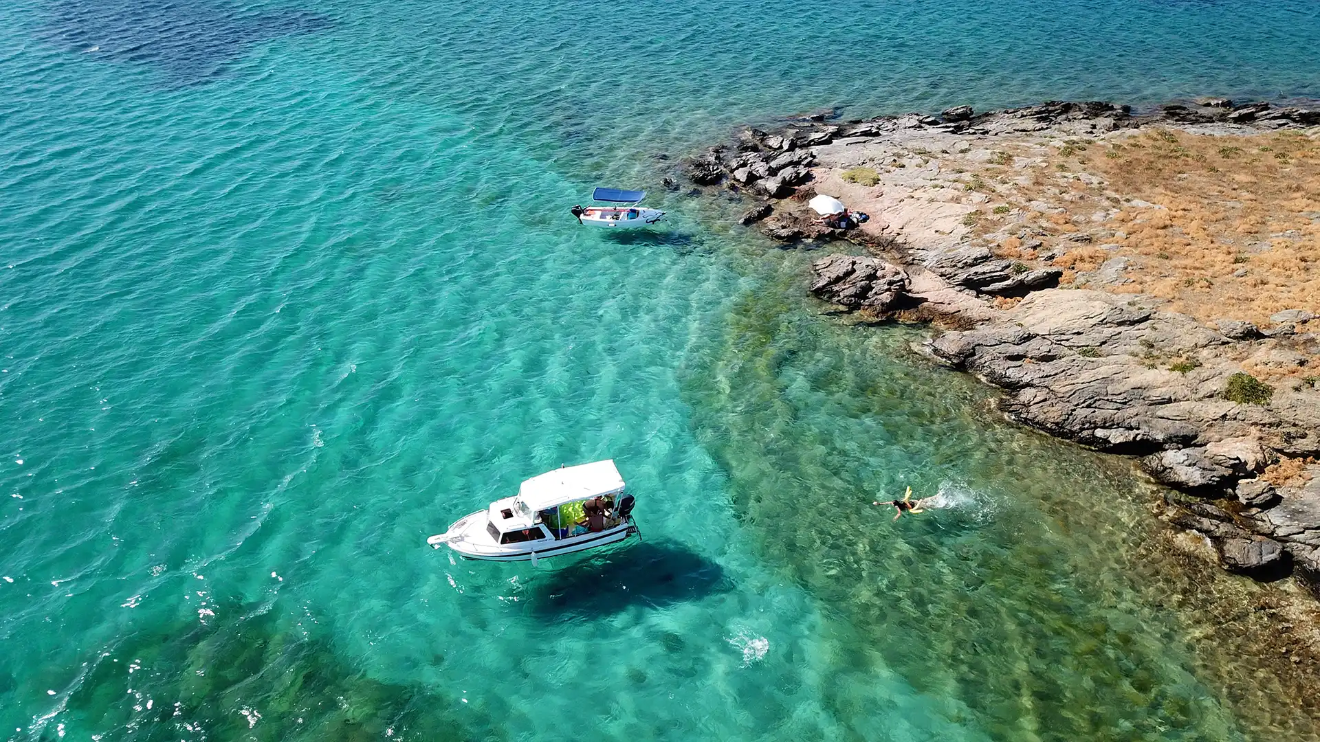 Aerial drone bird's eye view photo from boats docked in turquoise clear water rocky beach in island of Irakleia, Cyclades, Greece